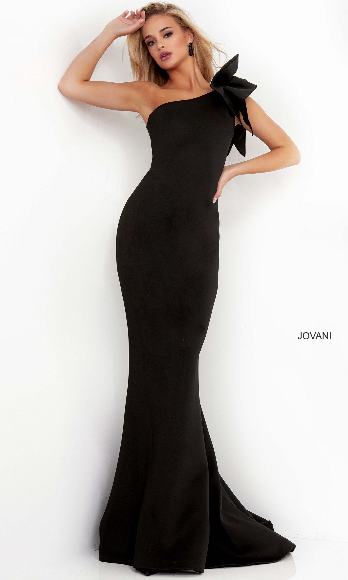 A woman poses against a white background in the black Jovani 32602 one-shoulder mermaid prom gown, featuring a dramatic bow detail and exuding elegant evening style.